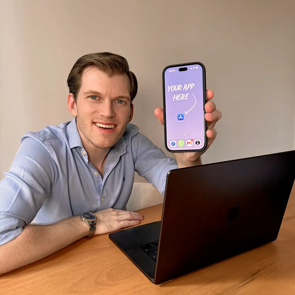 Philippe at his desk, holding a phone with a new app icon on the home screen.